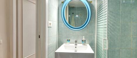 Un bagno con un lavandino bianco, uno specchio con cornice blu e una doccia con porta in vetro.
