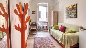 Un espacio habitable compacto con un sofá, una mesa de comedor, sillas, un tapete estampado, un cuadro y vistas a través de una puerta.
