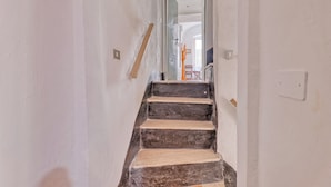Una escalera conduce a una habitación con paredes blancas, una puerta visible y un interruptor de luz en la pared.
