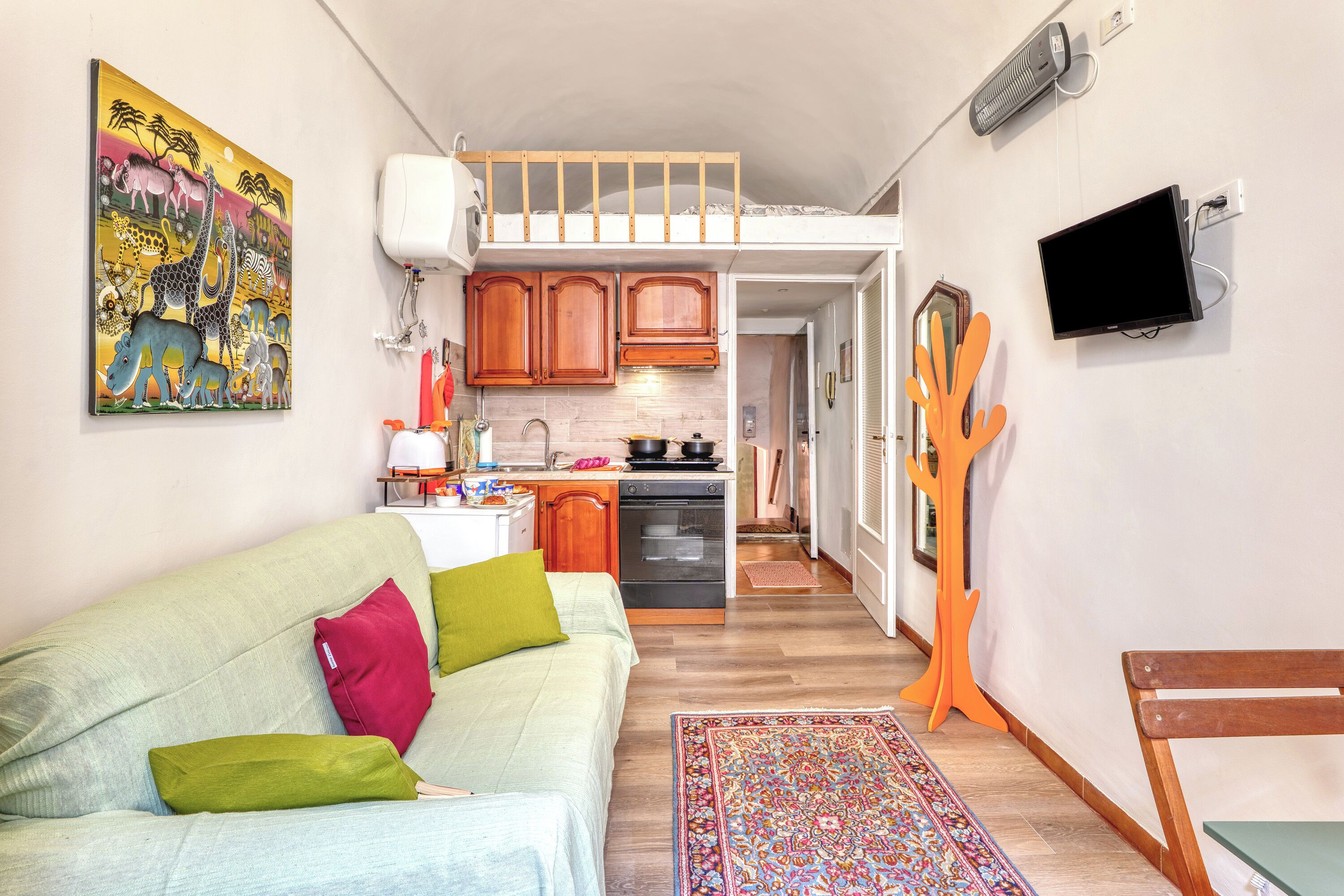 A compact living space with a kitchenette, a sofa with cushions, a television, and a colorful rug.