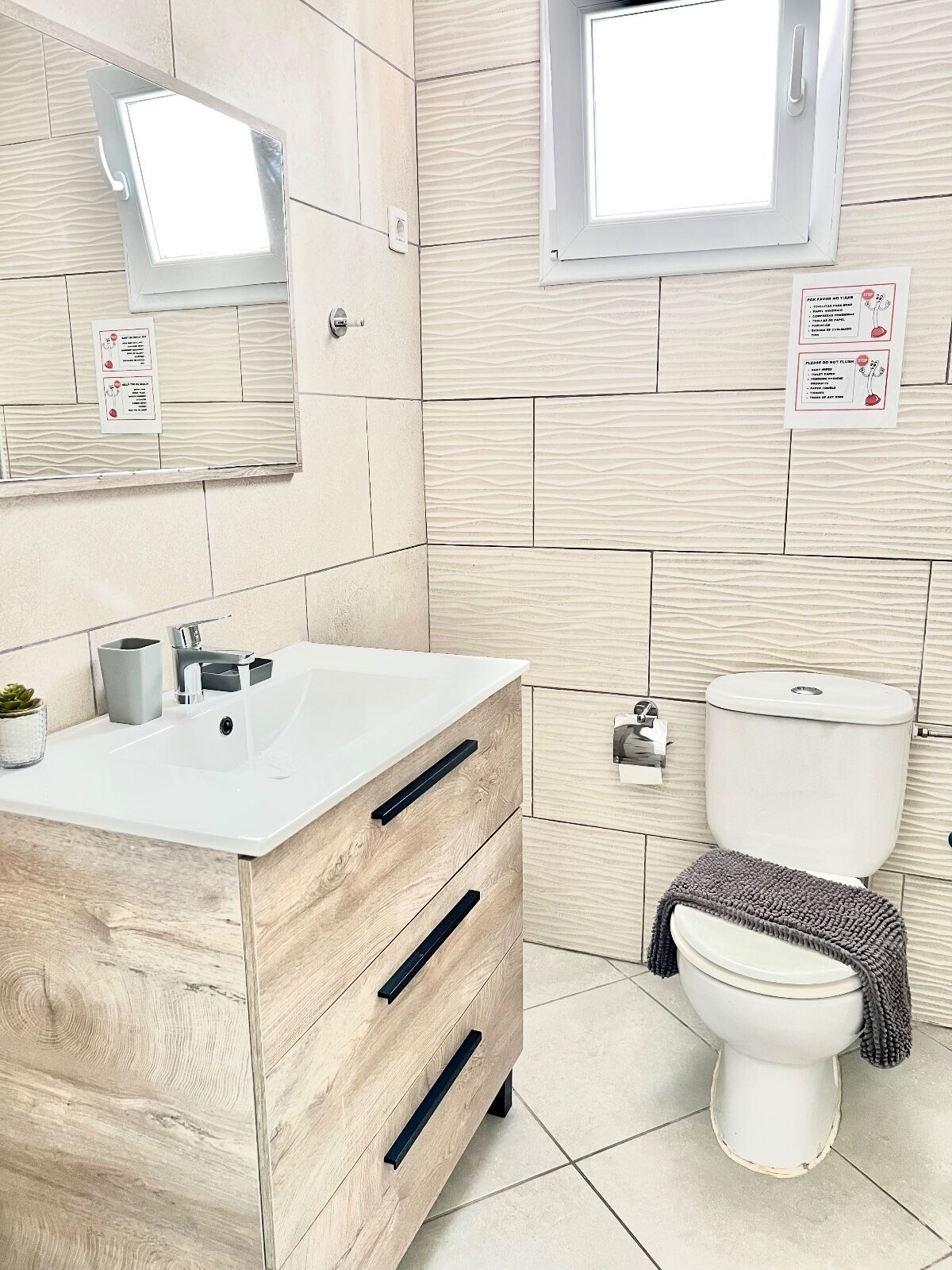 Ein Badezimmer mit einem Holzbadschrank, einem weißen Waschbecken, einem Spiegel, einer Toilette und einem Fenster.