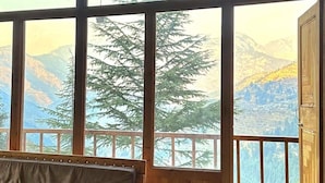 A room with a wooden bench, large windows, and a view of mountains. - Ruhaani Cottages And Cafe (Banjar)