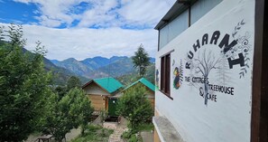 A building with a sign for 'THE COTTAGES TREEHOUSE & CAFE' against a backdrop of mountains. - Ruhaani Cottages And Cafe (Banjar)
