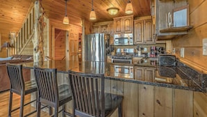 A wooden cabin interior with a kitchen featuring a stainless steel refrigerator, wooden cabinets, and a bar area with chairs.