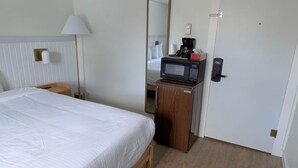 A hotel room with a bed, a nightstand, a lamp, a microwave, a coffee maker, and a door. - King Room - K (Lake Placid)
