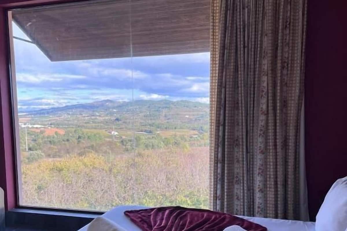 A hotel room with a large window offering a view of a hilly landscape.