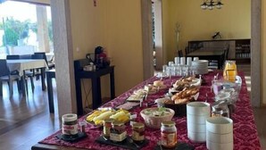 A breakfast buffet with various food items and condiments on a long table, set in a room with yellow walls and a wooden floor. - Tranca da Barriga by Quinta De São Tiago (Covilha)