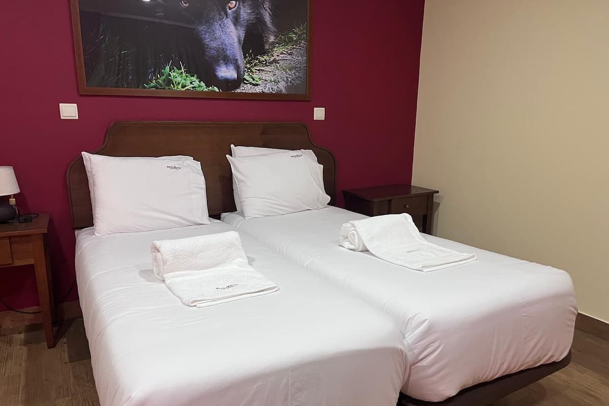 A double bed with white linens and two pillows, a nightstand with a lamp, and a framed picture of a gorilla on the wall.