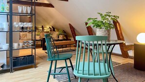 A cozy loft-style room with a wooden ceiling, a teal chair, a small round table, and a shelving unit with glassware and dishes. - Cozy apartment in Borås with WiFi (Borås)