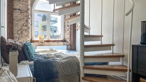 A bedroom with a bed, a wooden staircase, a radiator, and a window with a view of buildings. - Cozy apartment in Borås with WiFi (Borås)