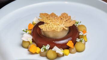 A dessert on a white plate with a central spherical dessert, surrounded by small round items and garnished with flowers and leaves.