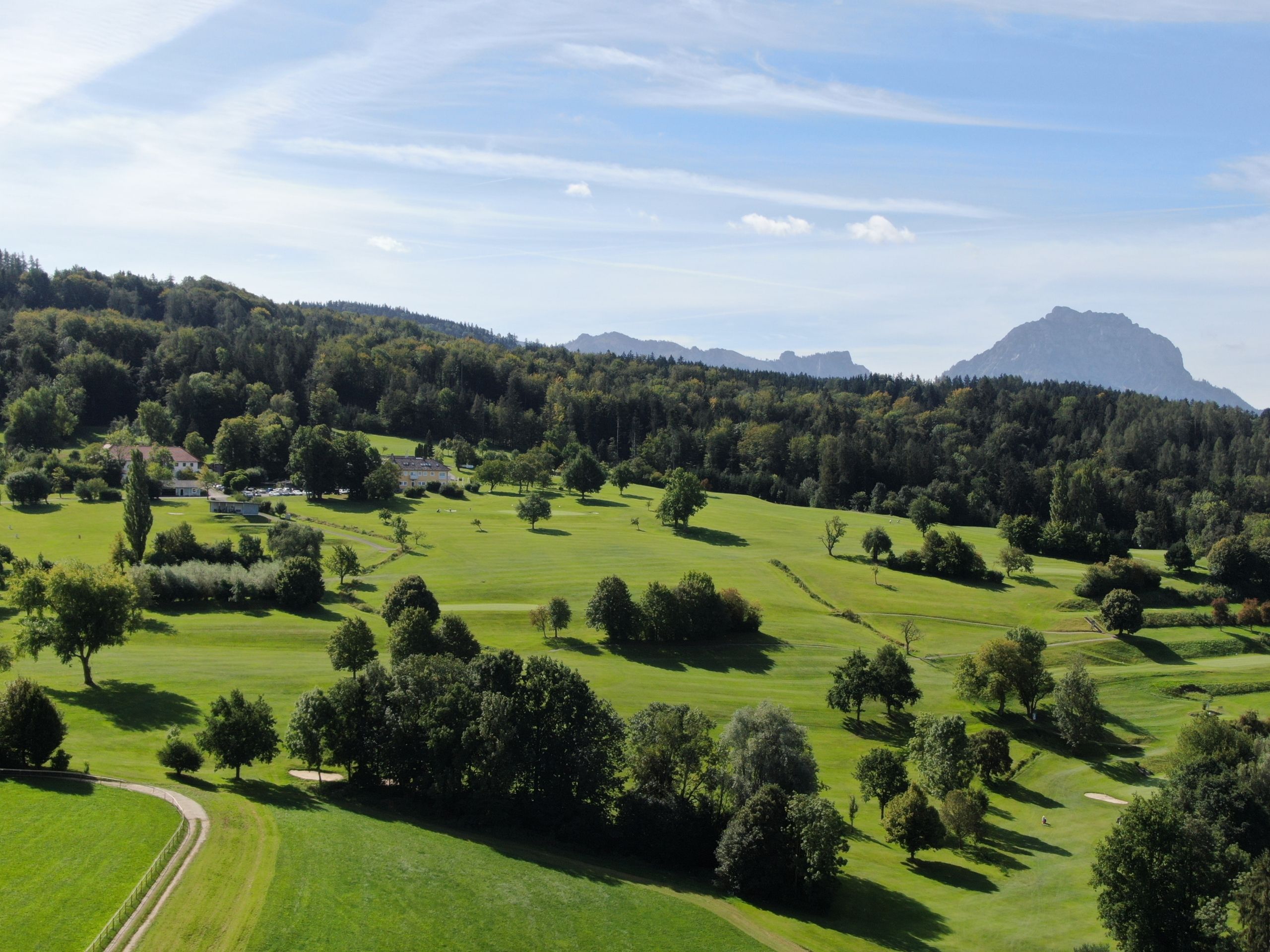 A golf course with a clubhouse, trees, and a mountain in the background.