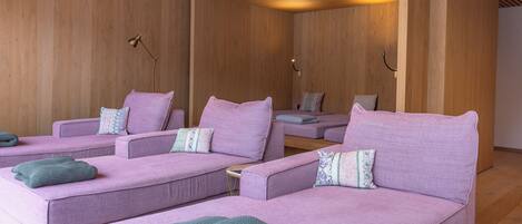 Ein moderner Spa-Raum mit drei lilafarbenen Sofas, jeweils mit einer grünen Decke.