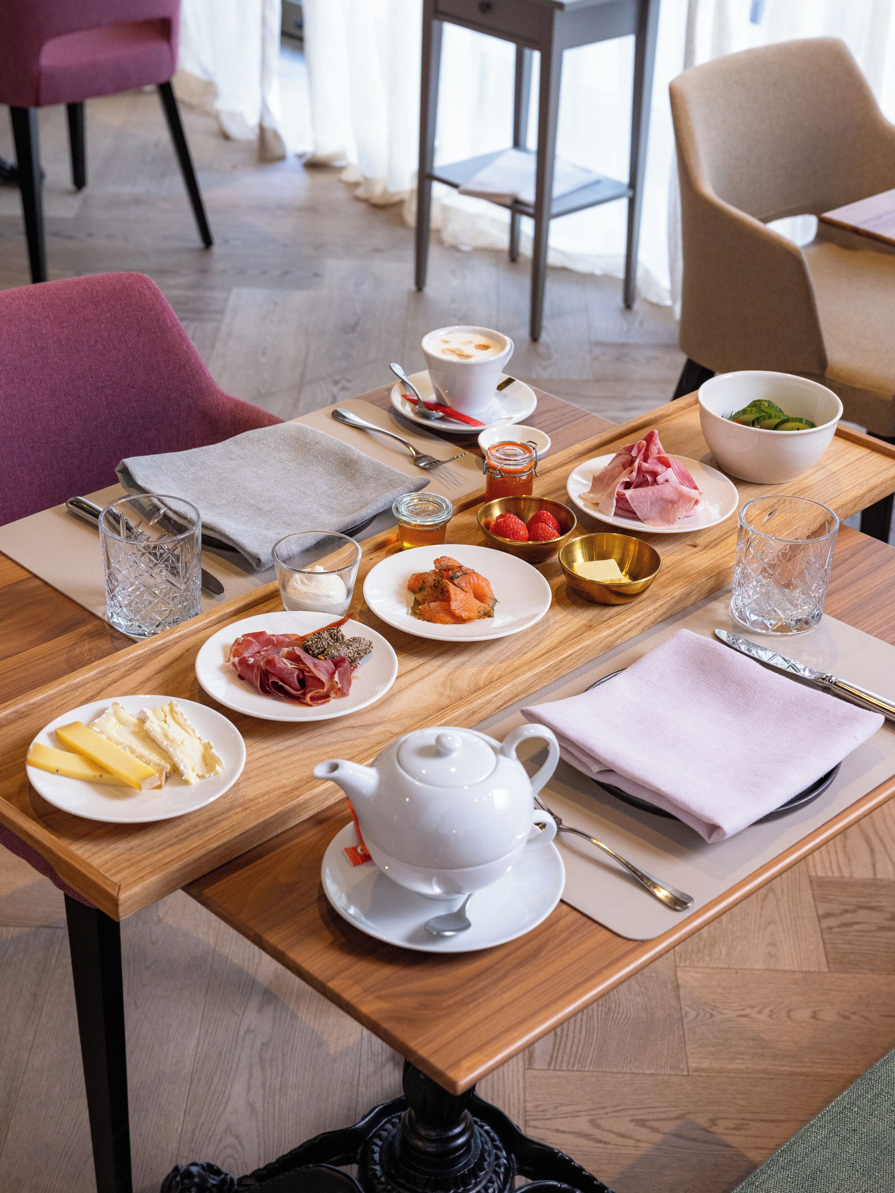 A breakfast table with plates of food, a teapot, and various condiments.
