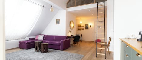 A loft-style bedroom with a sloped ceiling, a purple sofa, a wooden ladder, and a desk area.