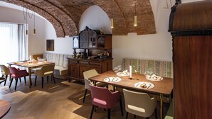 A dining area with wooden tables and chairs, a brick ceiling, and hanging pendant lights. - Boutique Hotel Zum Goldenen Hirschen (Gmunden)