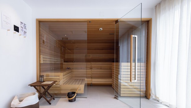 A modern sauna room with wooden benches, a small table, and a basket. - Boutique Hotel Zum Goldenen Hirschen (Gmunden)