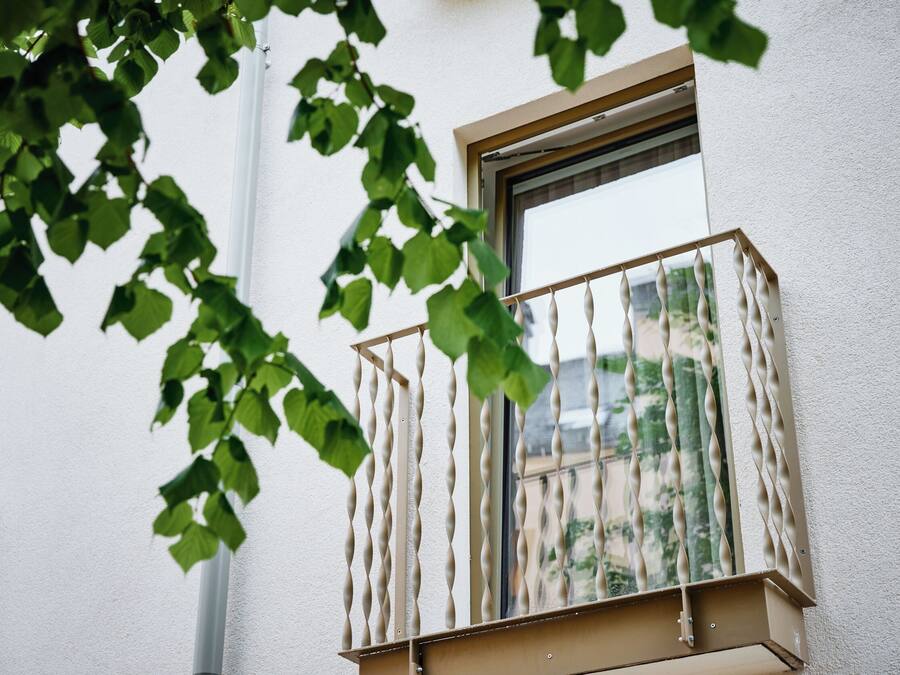 Une fenêtre dotée d’un garde-corps en métal torsadé original et offrant une vue sur la verdure environnante.