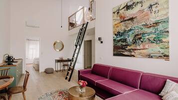 A modern living room with a purple sofa, a round coffee table, and a large abstract painting on the wall.