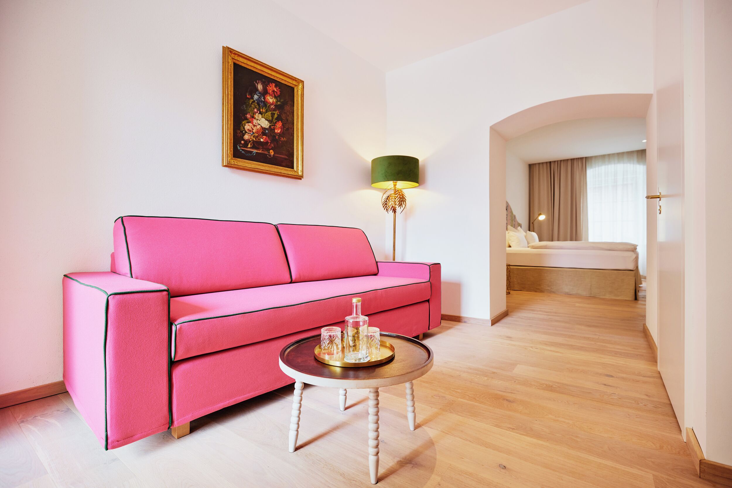 Un canapé rose, une table basse ronde avec un plateau, une lampe et un tableau au mur.