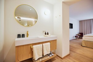 Un baño moderno con un espejo redondo, una encimera blanca, un mueble de madera y un par de toallas.