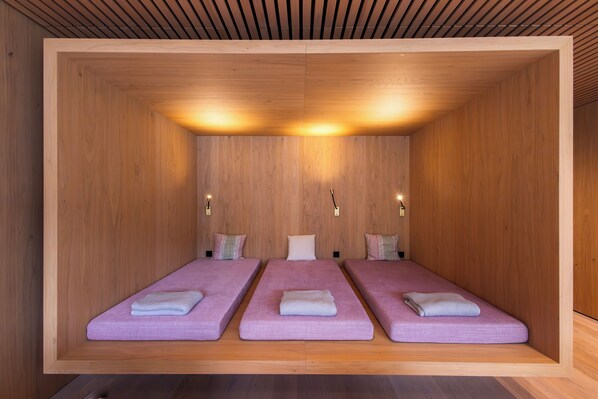 Una habitación con tres camas alineadas, paredes de madera y techo a listones.