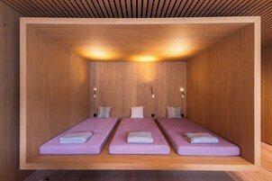 Una habitación con tres camas alineadas, paredes de madera y techo a listones.