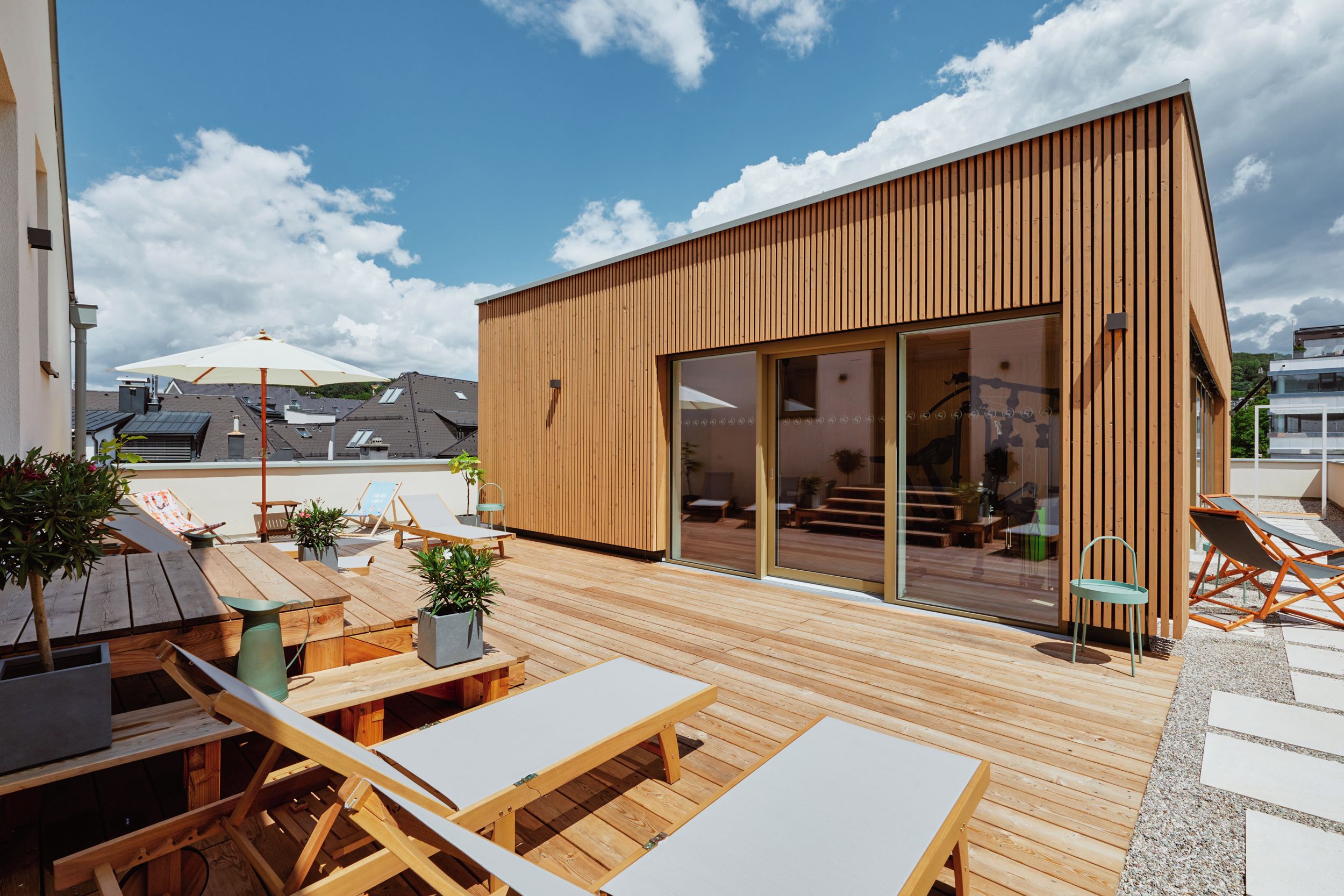 Una terraza moderna al aire libre con mobiliario de madera y un ventanal de vidrio que da a un espacio interior.
