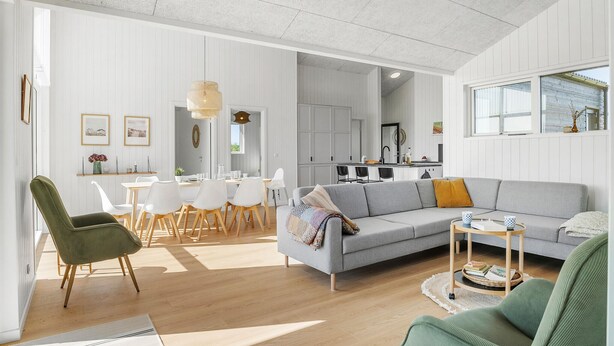 A spacious living area with a grey sofa, a dining table with chairs, and a kitchen in the background. - Stunning home in Jerup with sauna (Jerup)