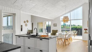 A modern kitchen with a central island, white cabinetry, and a large window overlooking a garden. - Stunning home in Jerup with sauna (Jerup)