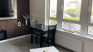 A dining area with a table and chairs, a flat-screen TV mounted on the wall, and a window with a view of the street.