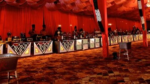 A banquet hall with tiered red drapery, chandeliers, and a long table with a patterned tablecloth.