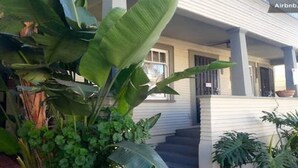 Et hus med en veranda, store grønne planter og en trappe op til indgangen.