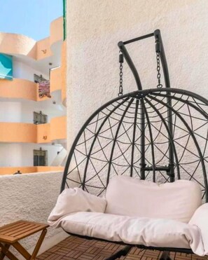 Una silla colgante con diseño geométrico, un asiento acolchado y una pequeña mesa de madera a su lado.
