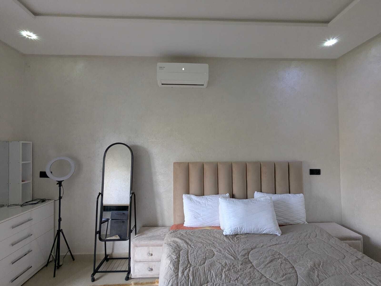 Une chambre à coucher comprenant un lit, une commode, une coiffeuse avec un miroir et un climatiseur fixé au mur.