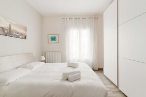 Una habitación de hotel con una cama, un cuadro de paisaje urbano, una fotografía enmarcada y cortinas de gasa.