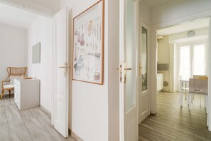 Una habitación con una puerta blanca, un cuadro en la pared, una silla de madera y una pequeña mesa.