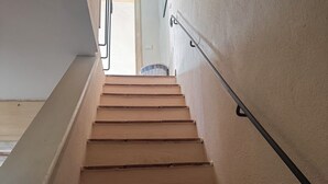 Un escalier avec des marches en bois et une rampe, menant à une pièce dotée d’une porte et d’un panier posé sur le sol.