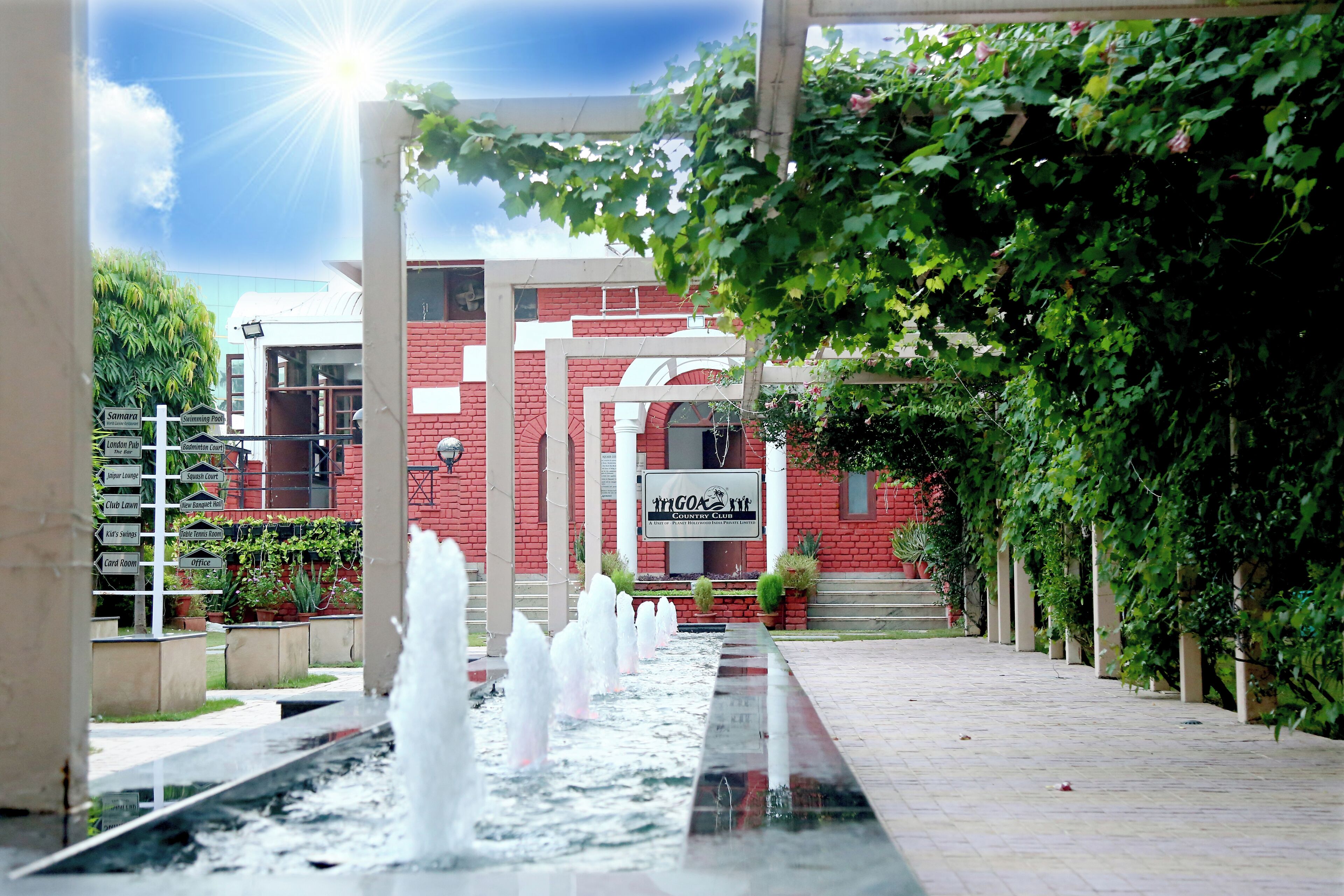 A courtyard with a water feature, a red building with a sign, and greenery.