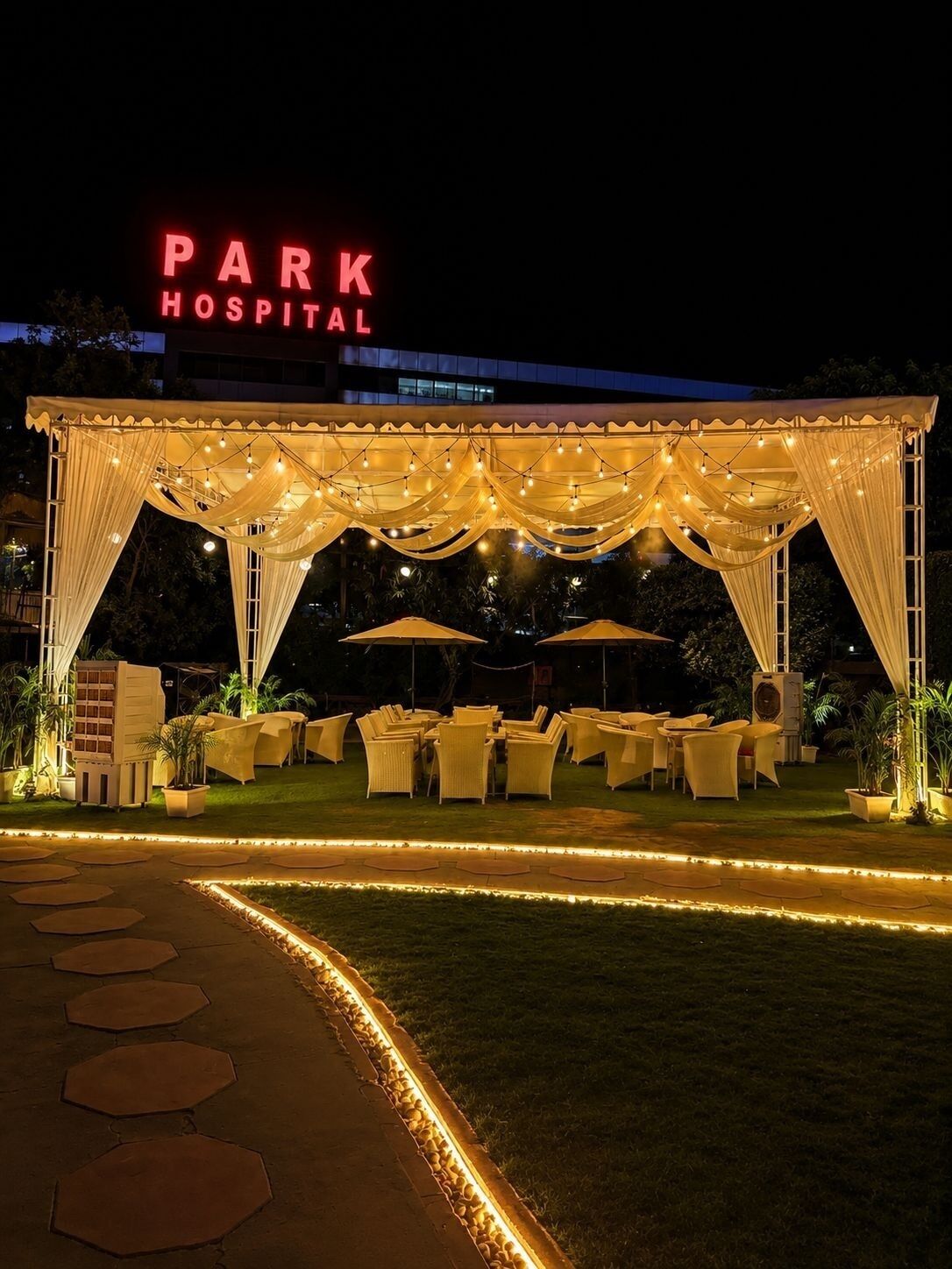 An outdoor event space with a marquee, tables, chairs, and string lights.