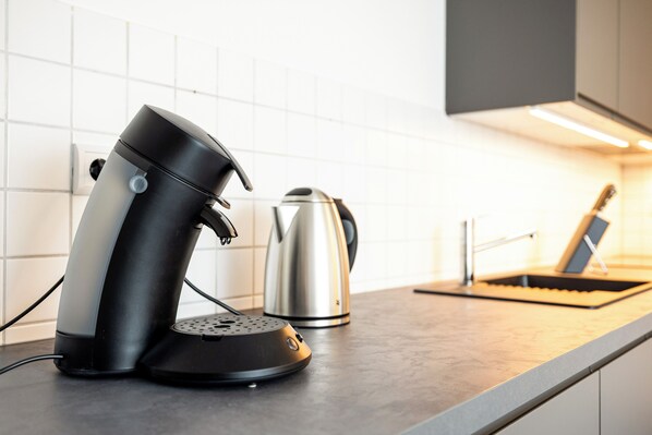 A kitchen with a coffee maker, kettle, and a laptop on the counter. - NORA Dresden Hauptbahnhof (Dresden)