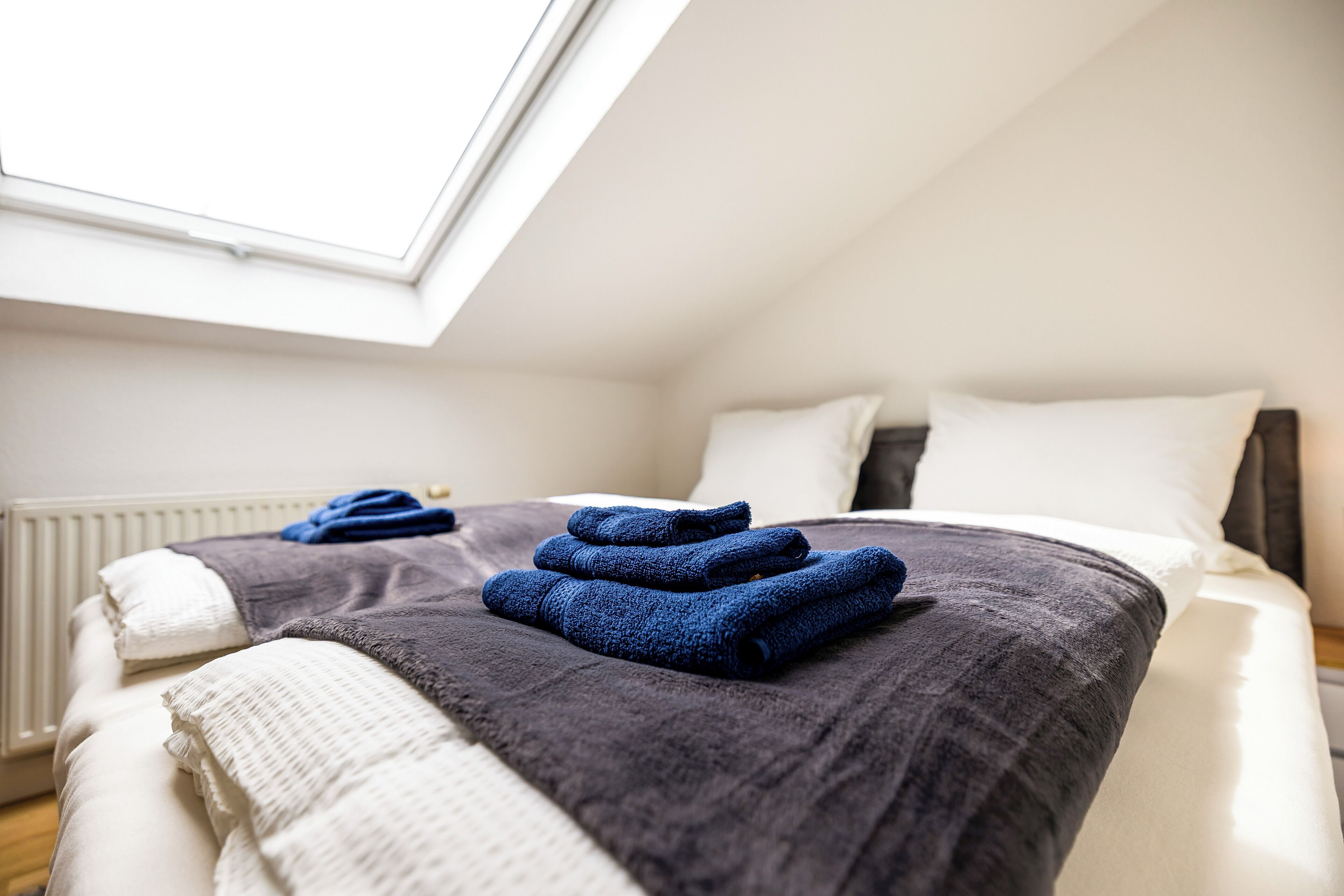 Un lit bien fait, avec une couette grise et blanche, une serviette bleue et un oreiller blanc.