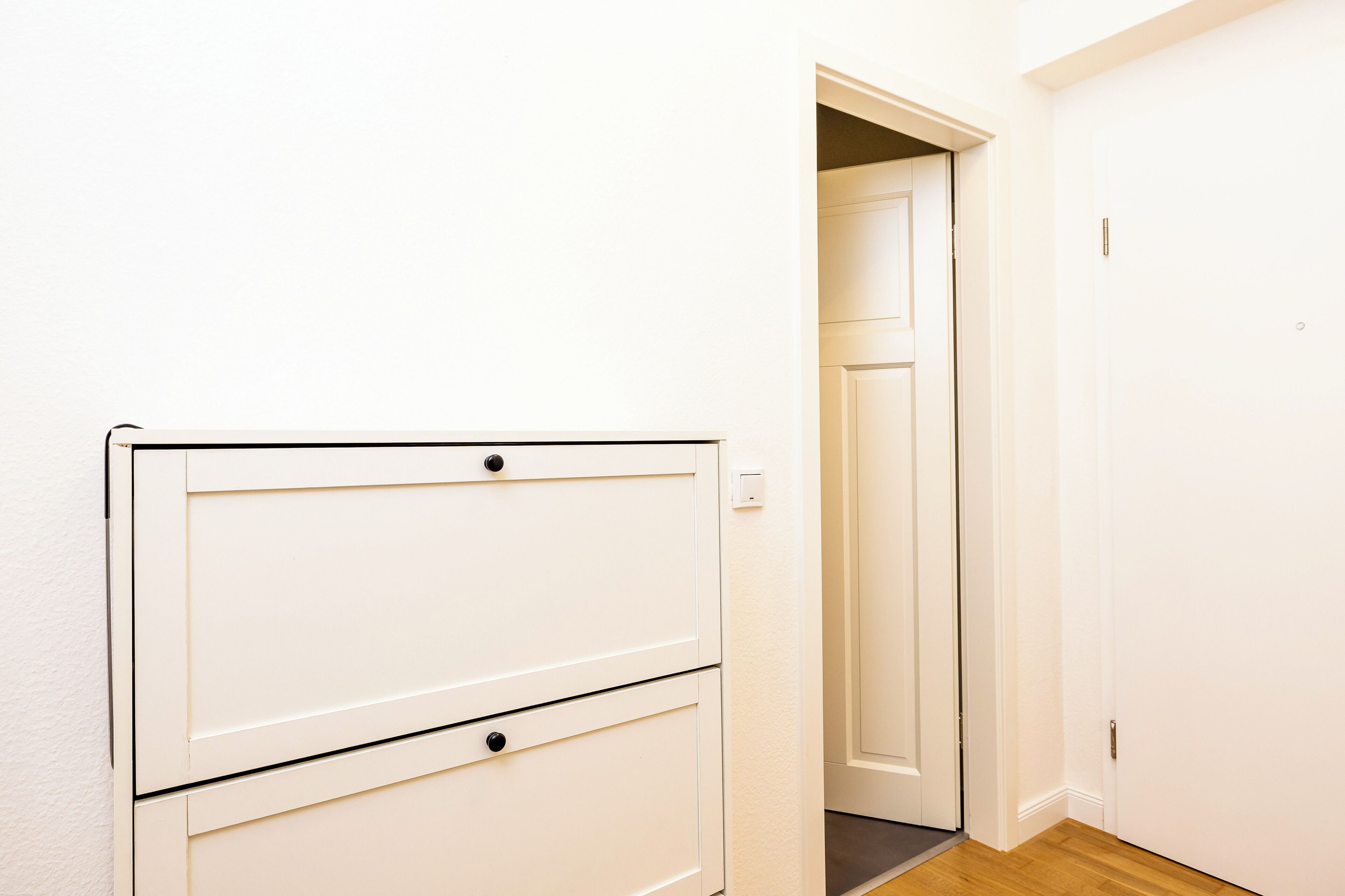 A white wall with a white cabinet and a door leading to another room.