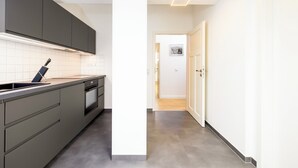 A modern kitchen with grey cabinets, a built-in oven, and a sleek countertop. - NORA Dresden Hauptbahnhof (Dresden)