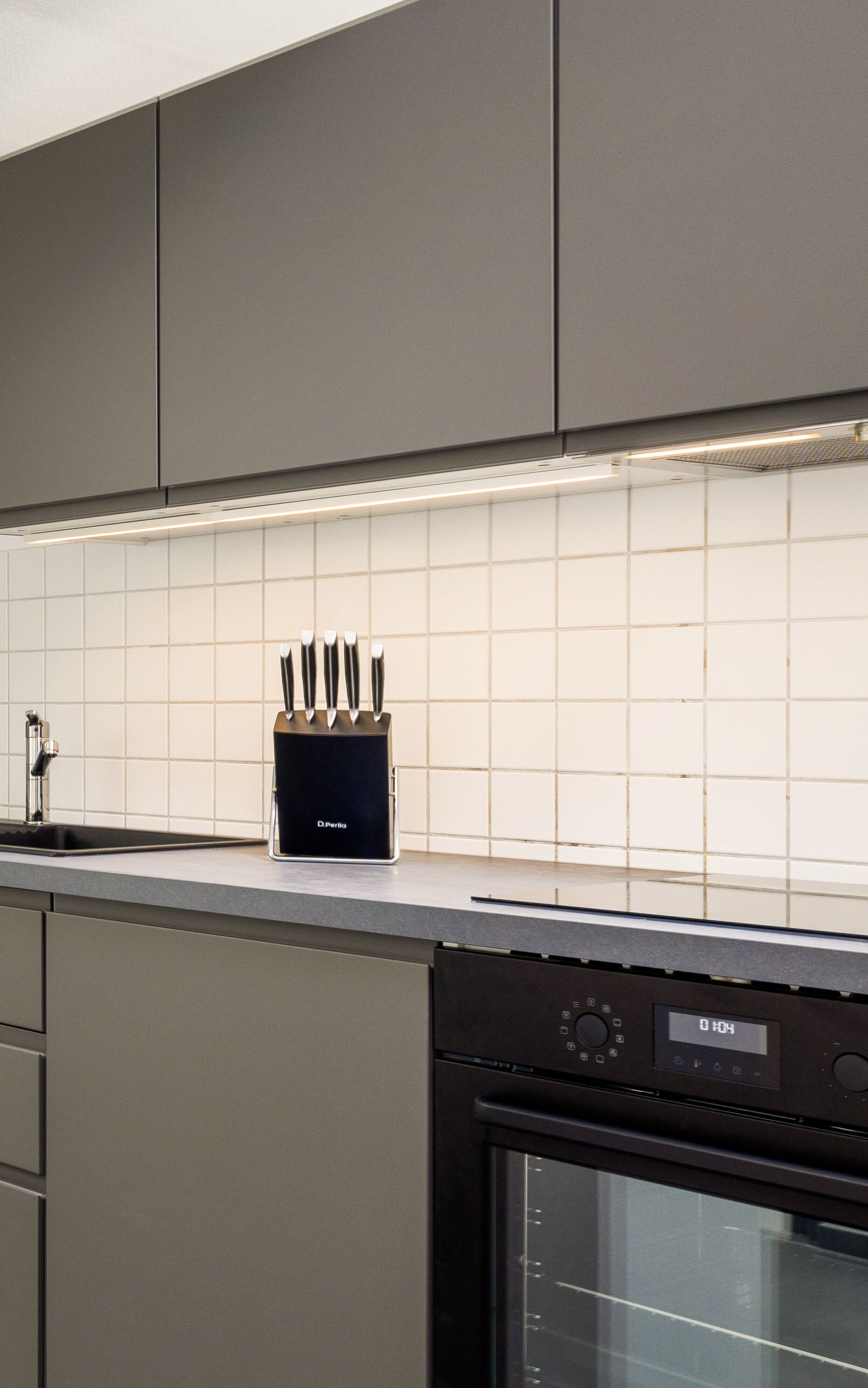 Una cocina moderna con armarios grises, un bloque de cuchillos negros y un horno empotrado.