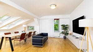 A modern living room with a dining area, skylights, a large TV, and a potted plant. - NORA Dresden Hauptbahnhof (Dresden)
