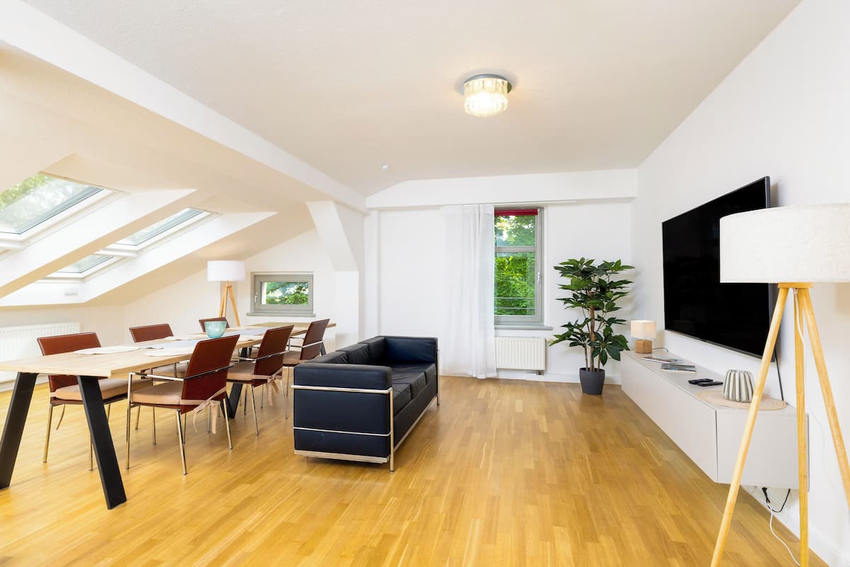 Een moderne woonkamer met een eethoek, dakramen, een grote televisie en een potplant.