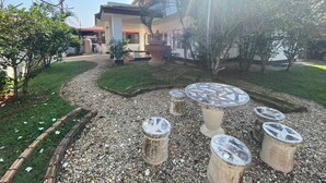 Un jardín con una mesa de piedra y taburetes, un sendero y un edificio con tejado rojo al fondo.