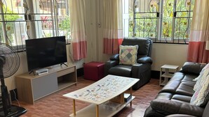 Una sala de estar con un sofá, un televisor, una mesa de centro y un ventilador.