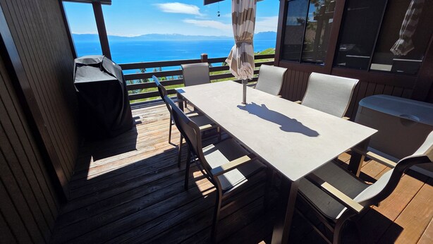 Une terrasse en bois avec une table et des chaises, offrant une vue panoramique sur l’océan.
